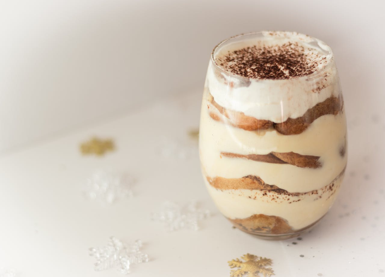 Close-up of a creamy tiramisu dessert in a glass, beautifully presented with cocoa topping, perfect for tasty indulgence.